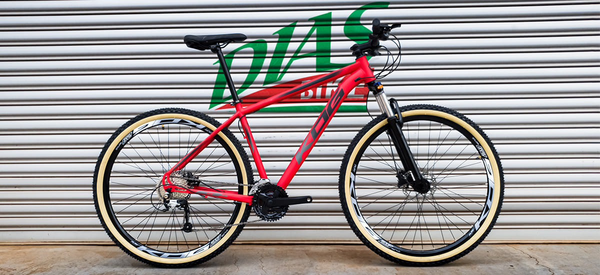Bicicleta vermelha com pneu de faixa bege escorada em uma parede com o logo da dias bike