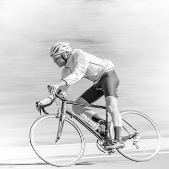 Pessoa pedalando com trajes de ciclista, capacete, imagem em preto e branco